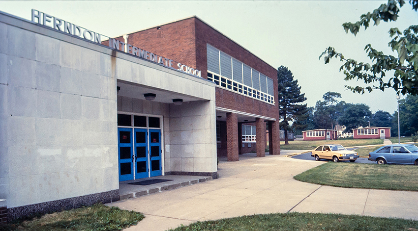 Color photograph of Herndon Middle School taken in the mid-1980s. The old 1927 building has been torn down and two mobile classrooms can be seen in the distance. The main entrance to the building is on the left.
