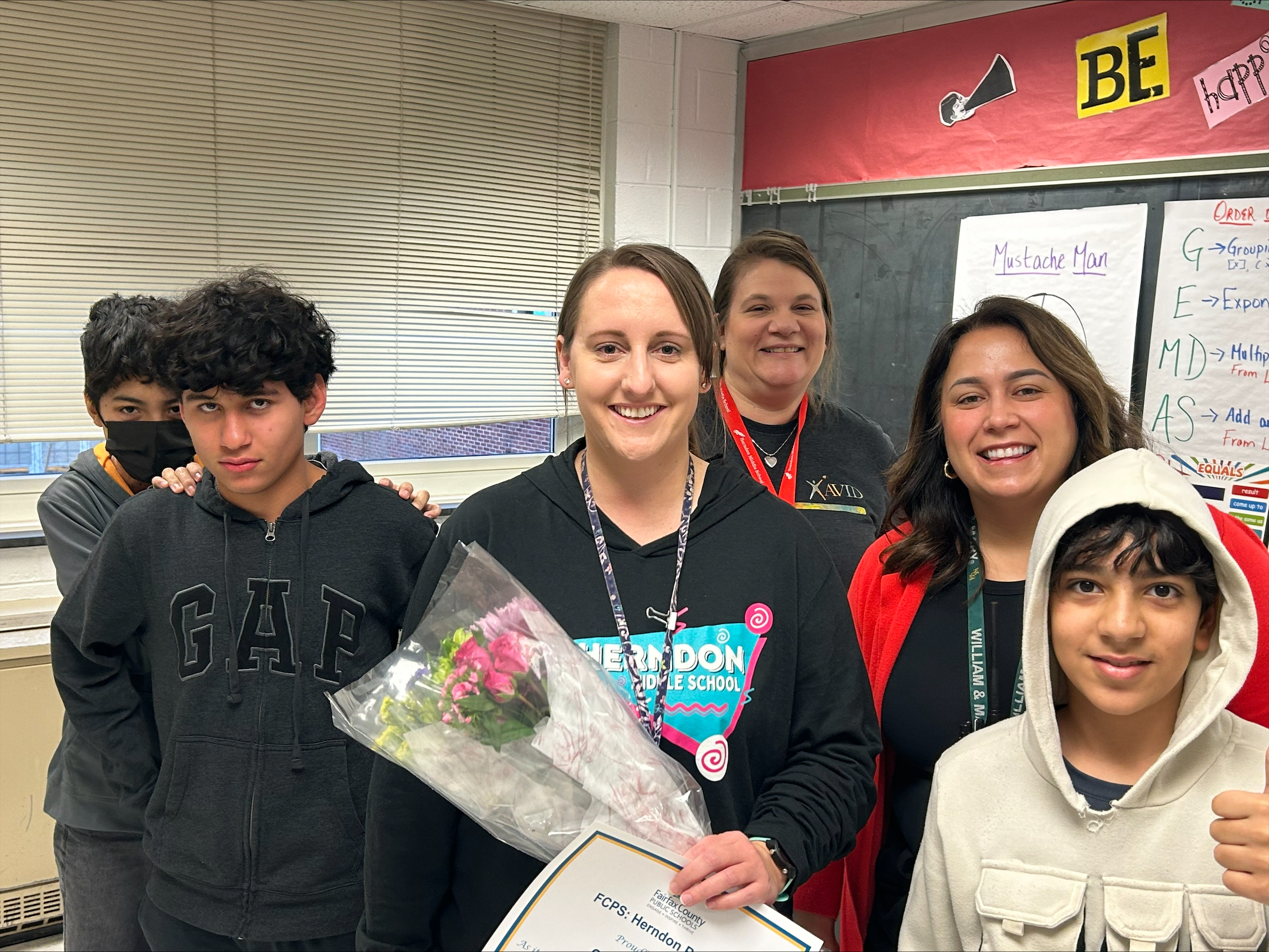 Caitlin Ferrence posing with a few students, her team teacher Ms. Carvil and Prinipal Vereb with her certificate and flowers