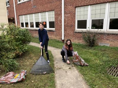 Two student volunteers rake leaves together at the School Clean Up